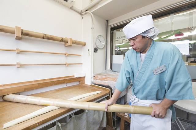 竹を使いテコの原理で麺を打って平たくしてゆく